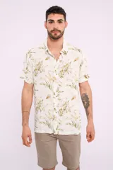 Camisa blanca con estampado de hojas verdes y marrones, de manga corta y cuello clásico.