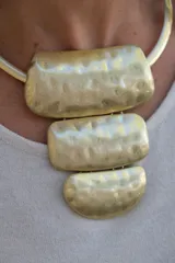 Collar rígido de metal dorado con diseño de gargantilla y tres dijes colgantes de formas rectangulares y semicirculares con acabado martillado.