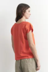 Remera naranja de corte recto, con cuello en V y mangas cortas. Presenta detalle de vainillas en los laterales y en los hombros.