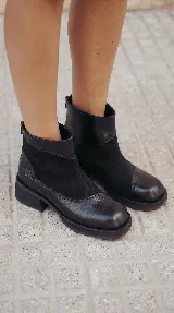 Bota corta de cuero negro con diseño de paneles que combina cuero liso y gamuza. Presenta puntera cuadrada, cierre trasero y suela con plataforma y taco bajo geométrico.