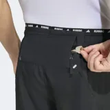 Short deportivo Adidas 2 en 1 con calza interior integrada, diseñado para running. Presenta un diseño en color negro con las icónicas tres tiras de la marca en tono claro sobre el muslo y logo en la cintura. Incluye cintura elástica con cordón de ajuste y bolsillos laterales con cierre.