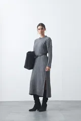 Vestido midi de punto en color gris, con diseño de tejido acanalado vertical, cuello redondo y mangas largas. Presenta una silueta recta y fluida.