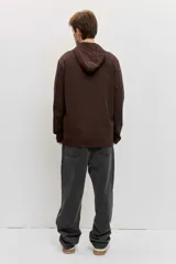 Buzo de friza de algodón marrón con capucha, cuello tipo polo con botones y un bolsillo frontal con solapa en el pecho.