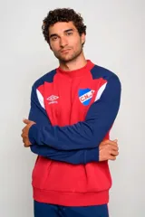 Buzo deportivo Umbro del Club Nacional de Football, color rojo con mangas azul marino y detalles blancos. Cuenta con cuello redondo y el logo de la marca y del club bordados en el pecho.