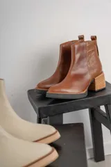 Bota corta de cuero negro con acabado combinado mate y charol. Presenta una tira decorativa con tachas metálicas y hebilla en el tobillo, tacón cuadrado robusto y suela con plataforma.