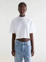 Remera cropped blanca de calce relajado, confeccionada en jersey de algodón, con cuello redondo acanalado y mangas cortas.