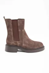 Bota tipo Chelsea de caña media, confeccionada en gamuza color marrón. Presenta paneles laterales elásticos al tono y una suela de goma robusta con plataforma baja y taco cuadrado.