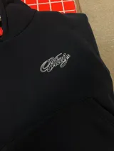 Hoodie negro con capucha y estampa gráfica blanca en la espalda con diseño tipográfico cursivo. Presenta puños y ruedo acanalados.
