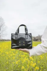 Mini bag negra de cuero charolado, con doble asa corta y logo grabado en el frente.