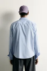 Camisa celeste de corte relaxed fit confeccionada en algodón, con cuello con botones y manga larga.
