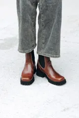 Bota tipo Chelsea de cuero color marrón, con paneles laterales elásticos en color negro y suela track robusta de goma negra.