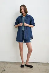 Camisa de jean azul, de corte holgado y manga larga, con cuello camisero y cierre frontal de botones oscuros.