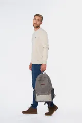Mochila gris de lona tipo canvas con detalles en beige. Tiene correas ajustables para los hombros, asa de mano, compartimento principal con cierre y bolsillo frontal.