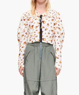 Blusa corta blanca con estampado de llamas anaranjadas, cuello con volados, mangas largas abullonadas y cierre frontal con broches.