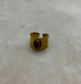 Anillo de banda ancha ajustable en tono dorado, con diseño de rayos grabados y una piedra central ovalada en color marrón.