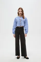 Blusa de corte holgado con estampado de cuadros vichy en azul y blanco, decorada con pequeños corazones rojos bordados. Presenta cuello a la base, mangas largas abullonadas y cierre frontal mediante cordones ajustables.