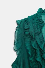 Blusa sin mangas color morado intenso, con escote en V profundo adornado con volantes fruncidos que recorren el frente y el cuello. Presenta cierre frontal con botones pequeños.