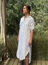Vestido camisero largo de lino blanco, con cuello camisero, manga corta enrollada y cierre frontal de botones de nácar. Presenta aberturas laterales en el bajo.