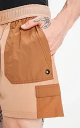 Short de baño de calce regular, color camel (marrón claro), con paneles de tela en tono marrón más oscuro en los bolsillos cargo laterales y en la parte superior de los bolsillos delanteros. Posee cintura elástica con cordón negro estampado.