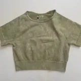 Remera deportiva verde oliva de corte cropped, con cuello redondo y mangas cortas.