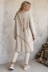 Sacon de lana color beige con diseño de paneles asimétricos, detalles en cintas de cuero y aplicaciones de tejido de punto grueso con trenzado. Presenta corte recto y largo midi.