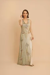 Vestido largo sin mangas de color crudo con bordados artesanales en canutillos y lentejuelas doradas y celestes, diseño de escote en V y silueta recta.