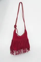 Cartera tipo bandolera color rojo oscuro, con flecos en la parte inferior y cierre de cremallera. Tiene una correa fina con un nudo decorativo.