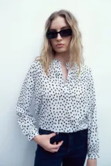 Blusa blanca con estampado floral negro, cuello mao y mangas largas con puños abotonados.
