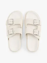 Sandalias planas de color blanco hueso con dos tiras ajustables mediante hebillas metálicas. Cuentan con una suela gruesa y dentada de plataforma.