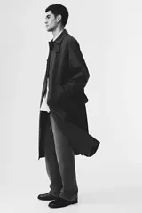 Gabardina estilo Mac de color marrón oscuro, confeccionada en sarga suave. Presenta cuello clásico, cierre frontal con botones ocultos, manga raglán con trabilla y botón en los puños, bolsillos insertados y cinturón extraíble para atar a la cintura. Tiene una abertura en la espalda y forro interior.