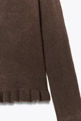 Jersey de punto color marrón con cuello redondo, manga larga y detalles de volantes en el cuello, puños y ruedo.