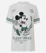 Remera blanca de algodón con cuello redondo y mangas cortas. Presenta un estampado frontal de Mickey Mouse con temática de tenis, rodeado por una corona de laureles, junto con detalles de rayas verdes en las mangas.