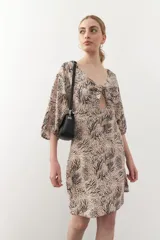 Vestido corto con estampado animal print en tonos beige y negro. Tiene mangas tres cuartos con elástico, cut-out en el frente y lazo.