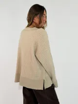 Sweater de tejido acanalado en color marrón oscuro, con cuello en V y detalles en tono metalizado en el cuello, puños y ruedo. Presenta un corte holgado y mangas largas.