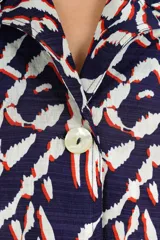 Camisa azul marino de manga corta, con cuello solapa, cierre frontal de botones y diseño estampado de estilo ikat en tonos blancos, rojos y azul marino.