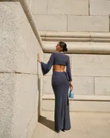 Vestido largo color verde esmeralda, con escote en V, corte a la cintura y falda con abertura lateral. Mangas largas acampanadas y espalda descubierta.