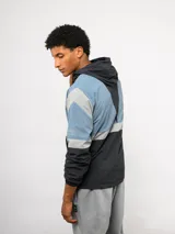 Campera de nylon Umbro con capucha, cierre frontal y diseño de bloques de color en gris, blanco y azul. Puños y dobladillo elásticos.