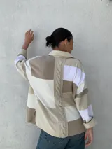 Camisa tipo chaqueta con diseño a rayas horizontales en tonos beige, blanco y marrón, con cuello camisero, cierre frontal con botones, mangas largas y bolsillos de cuero en el pecho.