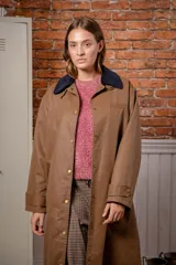 Trench larga de estilo encerado en color marrón, con cuello de pana en contraste y cierre frontal con botones a presión.