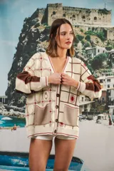 Cardigan oversized de tejido jacquard color crema con diseño de cuadrados en marrón y detalles bordados. Tiene cuello en V, cierre con botones, mangas largas y bolsillos frontales.