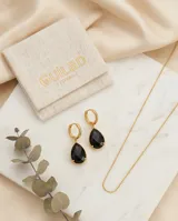 Caravanas colgantes de acero con baño de oro, compuestas por una argolla pequeña y un dije en forma de gota con piedra negra.