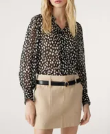 Camisa de manga larga con estampado de manchas blancas sobre fondo negro, confeccionada en tejido semitransparente. Presenta cuello clásico, cierre frontal con botones ocultos y puños abotonados.