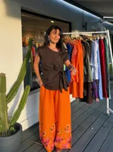 Pantalón ancho de tiro alto, color naranja vibrante, con estampado floral grande en tonos rosados y marrones en la parte inferior.
