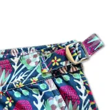 Short de baño con estampado floral y botánico en tonos violeta, rosa y verde sobre fondo oscuro. Presenta pretina fija con hebillas metálicas laterales para ajuste, cierre frontal con botón a presión, bolsillos laterales y bolsillo trasero.