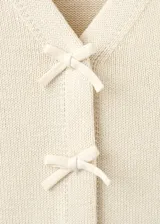 Cardigan de punto color beige, con escote en V y cierre frontal de botones con lazos decorativos.