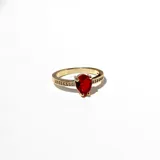 Anillo dorado con dije de cristal lágrima roja, con engarce de mesa y cristales claros alrededor.