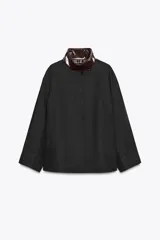 Chaqueta negra de la colección Zara Woman, confeccionada en hilatura con mezcla de algodón. Presenta un cuello alto brillante en contraste de color marrón oscuro, manga larga, bolsillos delanteros y pespuntes marcados. El forro interior es a contraste y el cierre frontal es con botones.