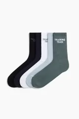 Pack de cinco pares de medias deportivas de caña media con tejido funcional absorbente. Presentan diseño acanalado en la caña, borde superior elástico y talón y punta reforzados. Incluyen el texto 'TRAINING TEAM' bordado en la parte superior.