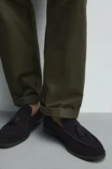 Mocasín de vestir negro confeccionado en piel con acabado serraje, con detalle de borlas en el empeine y ligero tacón.