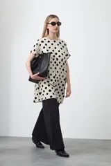 Vestido corto de silueta amplia con corte bajo busto, cuello a la base y mangas cortas. Presenta un estampado de lunares negros sobre fondo beige claro.